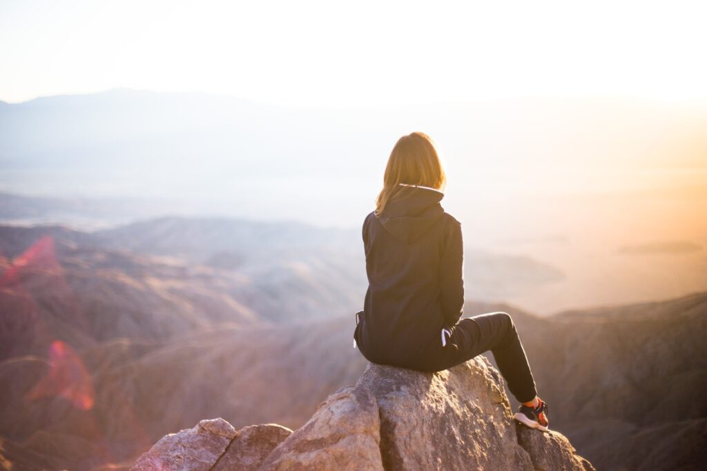 Symbolic image of hope and healing, person sitting on a mountain with a sunrise over mountains or light breaking through clouds